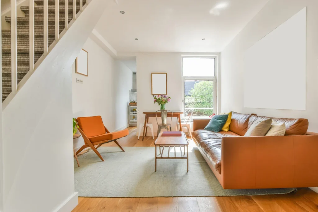 A modern living room with plants, furniture, large windows and orange couches