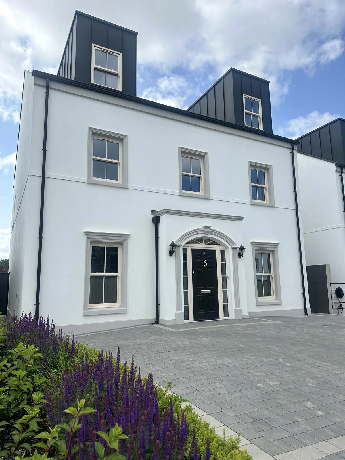 The outside of a large white house, with patio, garden and black front door