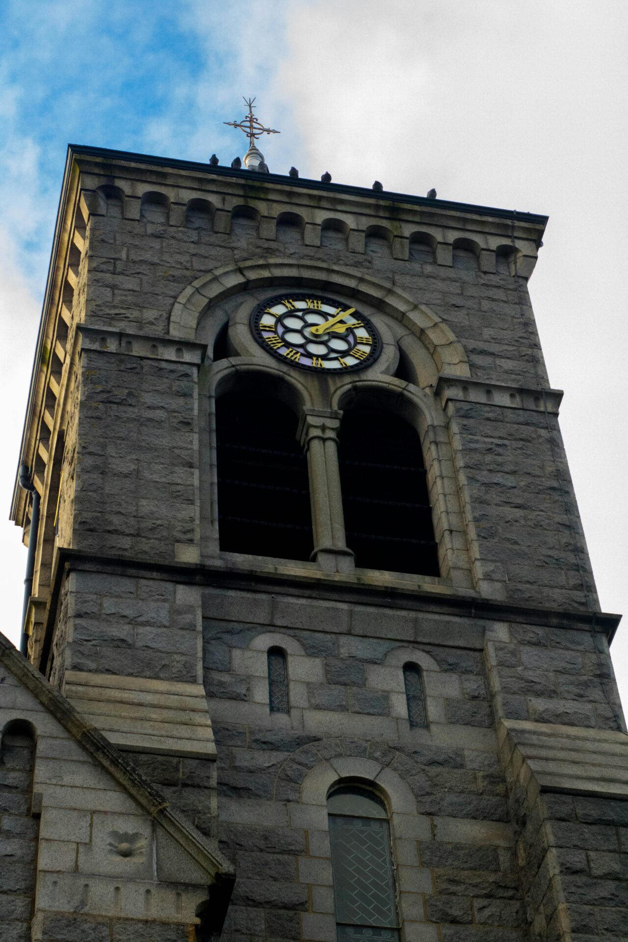 A clock tower with old stonework and a wind instrument atop